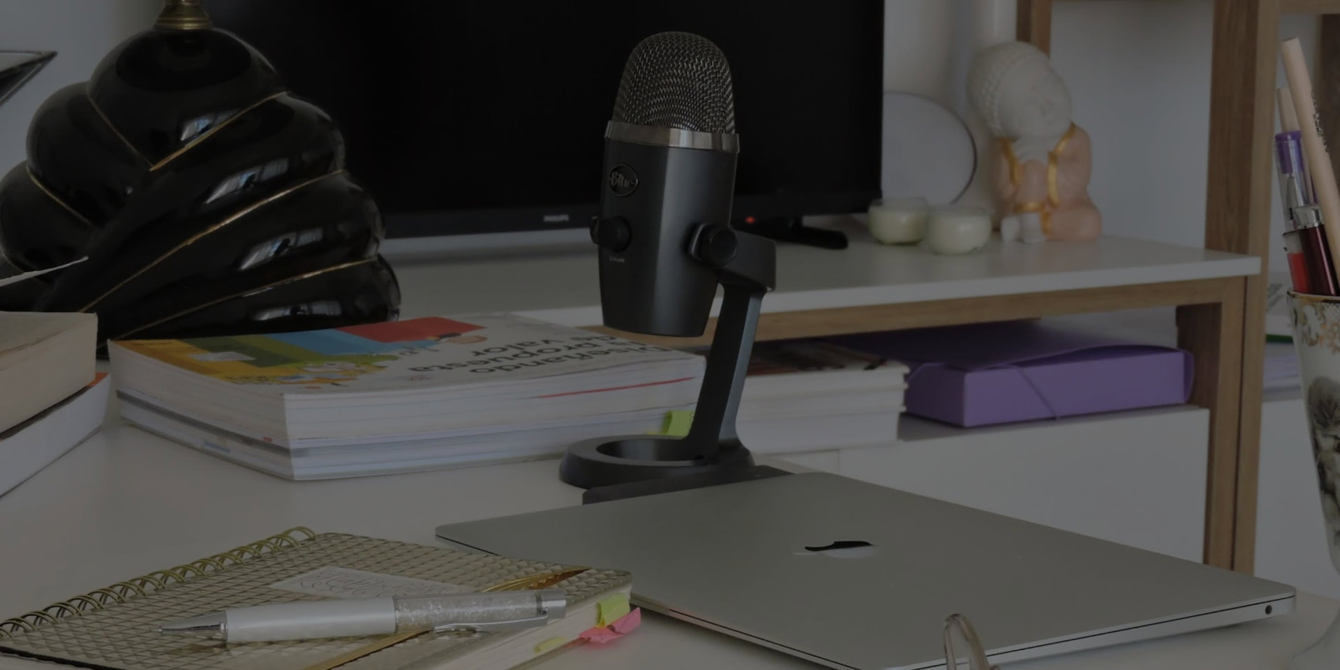 Micrófono de podcast sobre el escritorio, con una notebook y libros de fondo